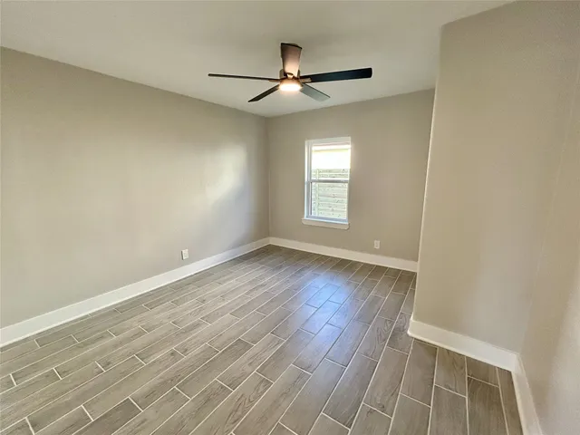 an empty room with wooden floor ceiling fan and windows
