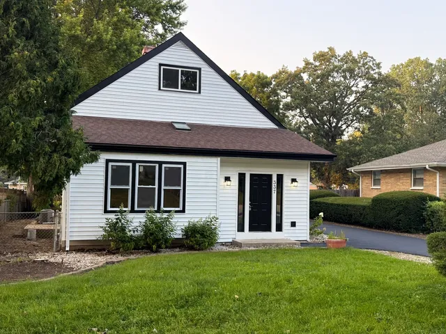 a view of a house with a yard plants and a large tree