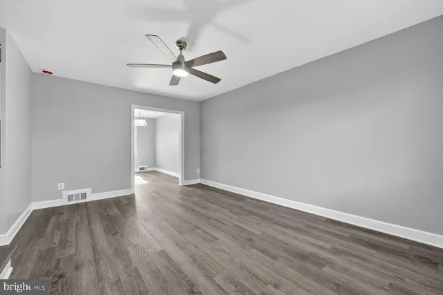 a view of an empty room with wooden floor and a ceiling fan