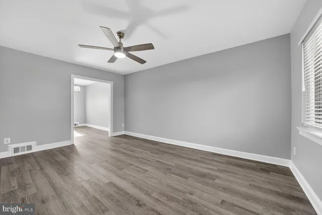 an empty room with wooden floor ceiling fan and windows