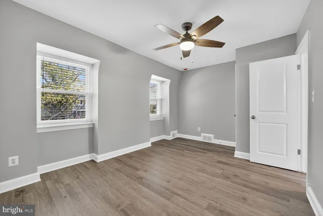 an empty room with wooden floor fan and windows
