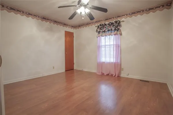 an empty room with wooden floor fan and windows