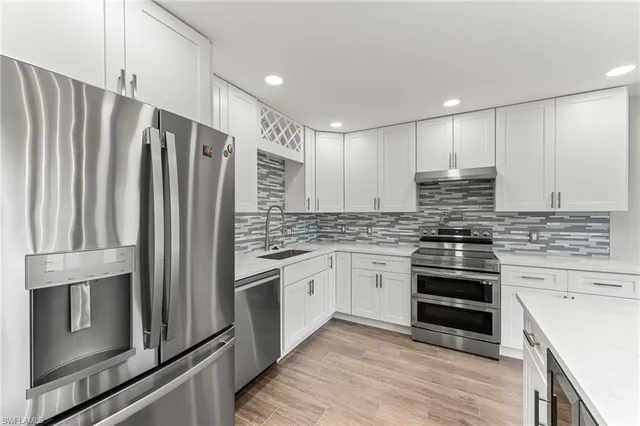 a kitchen with stainless steel appliances granite countertop a refrigerator a sink and white cabinets