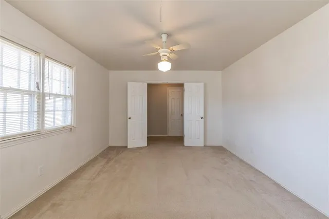 an empty room with chandelier fan and windows