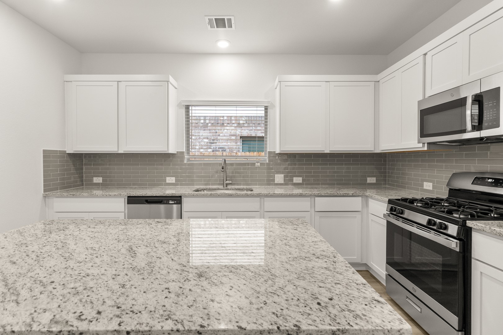 18605 Emu Lane Manor, TX 78653 - Photo 14 of 27 The kitchen features granite countertops, white cabinetry, a grey subway tile backsplash, and stainless steel appliances including a built-in microwave, gas range, and dishwasher