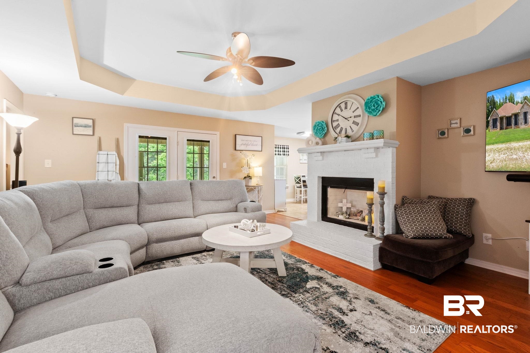 16151 Tolbert Road Bay Minette, AL 36507 - Photo 4 of 74 Living area featuring wood-finish flooring, a white brick fireplace with a mantle, a tray ceiling, and a ceiling fan with integrated lighting
