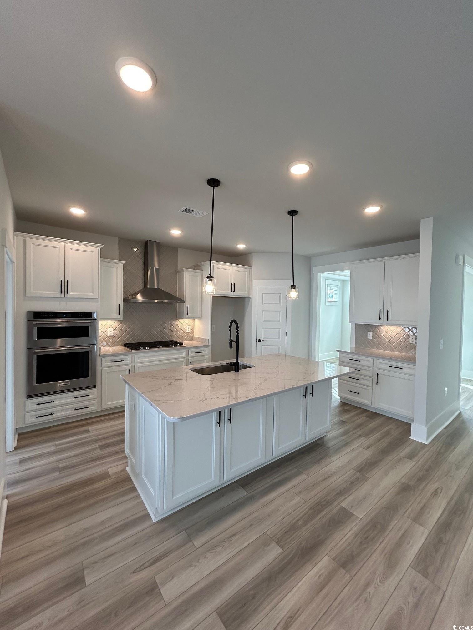 622 Braselton Lane Myrtle Beach, SC 29588 - Photo 4 of 15 Kitchen with double oven, gas cooktop, a sink, white cabinets, and wall chimney range hood