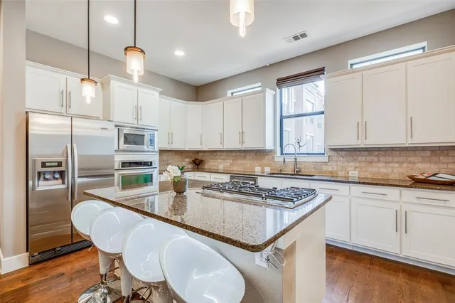 a kitchen with stainless steel appliances granite countertop a sink a stove a refrigerator cabinets and dining table