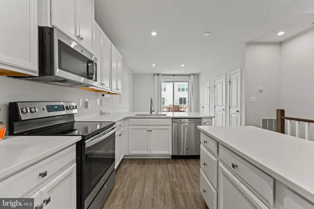 a kitchen with stainless steel appliances granite countertop a stove top oven a sink dishwasher and a refrigerator with wooden floor