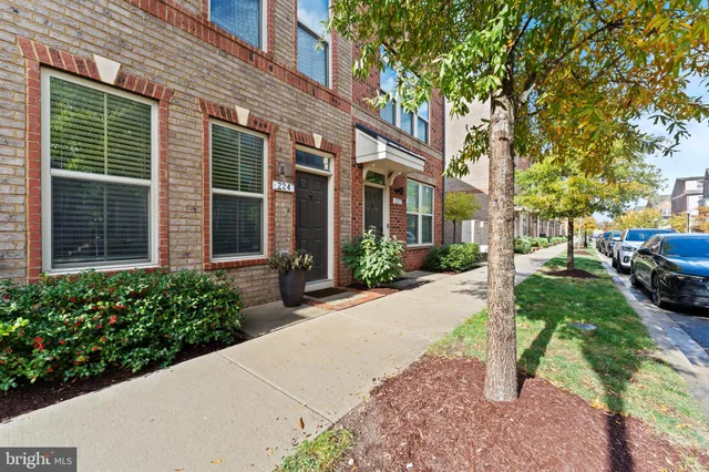 a view of a brick house with a yard plants and large tree