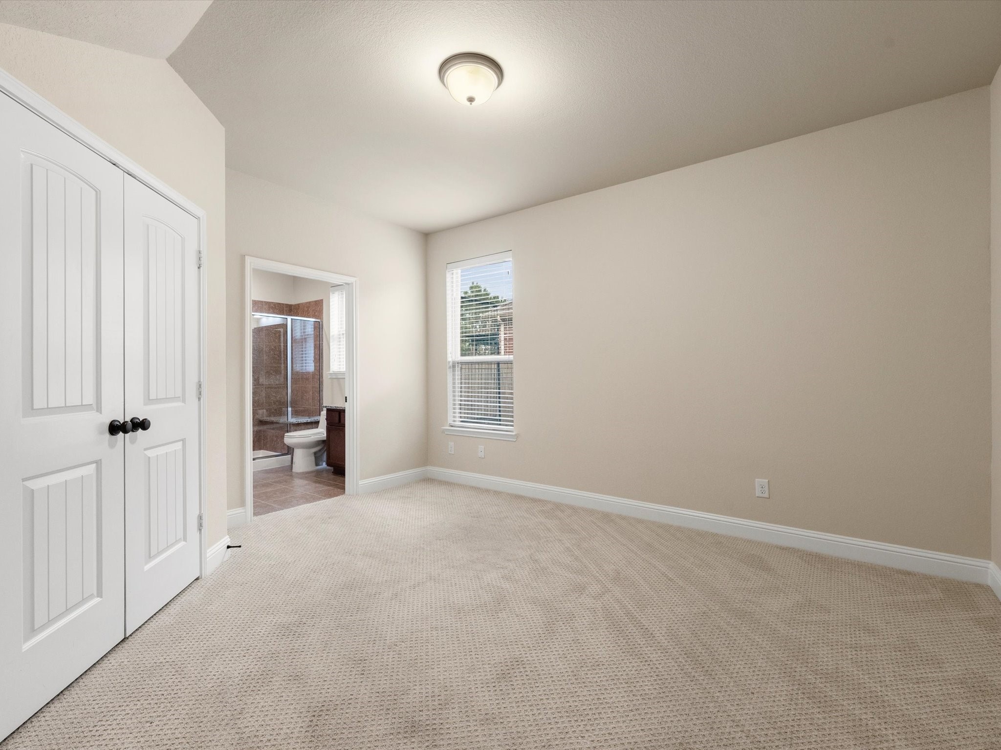 3907 Randle Ridge Court Fulshear, TX 77441 - Photo 24 of 46 This photo shows a bright, carpeted first floor private bedroom bath combo with a large walk-in closet and doorways that are extra wide. It includes a window for natural light, a closet with double doors, and an attached en-suite bathroom featuring a glass-enclosed shower.