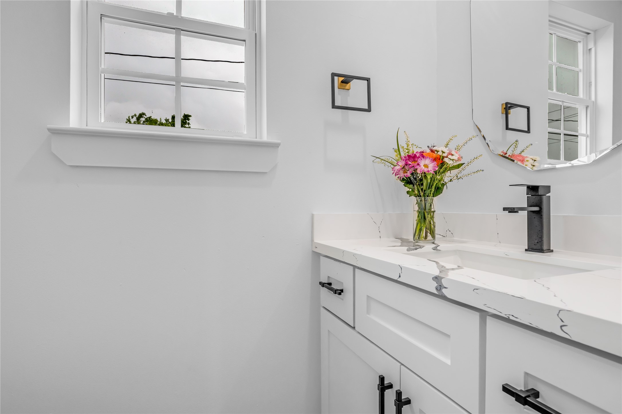 3168 Golfcrest Houston, TX 77087 - Photo 28 of 36 This elegant second bathroom exudes modern charm with its sleek white cabinetry, chic black accents, and a bright, airy feel enhanced by natural light from the window.