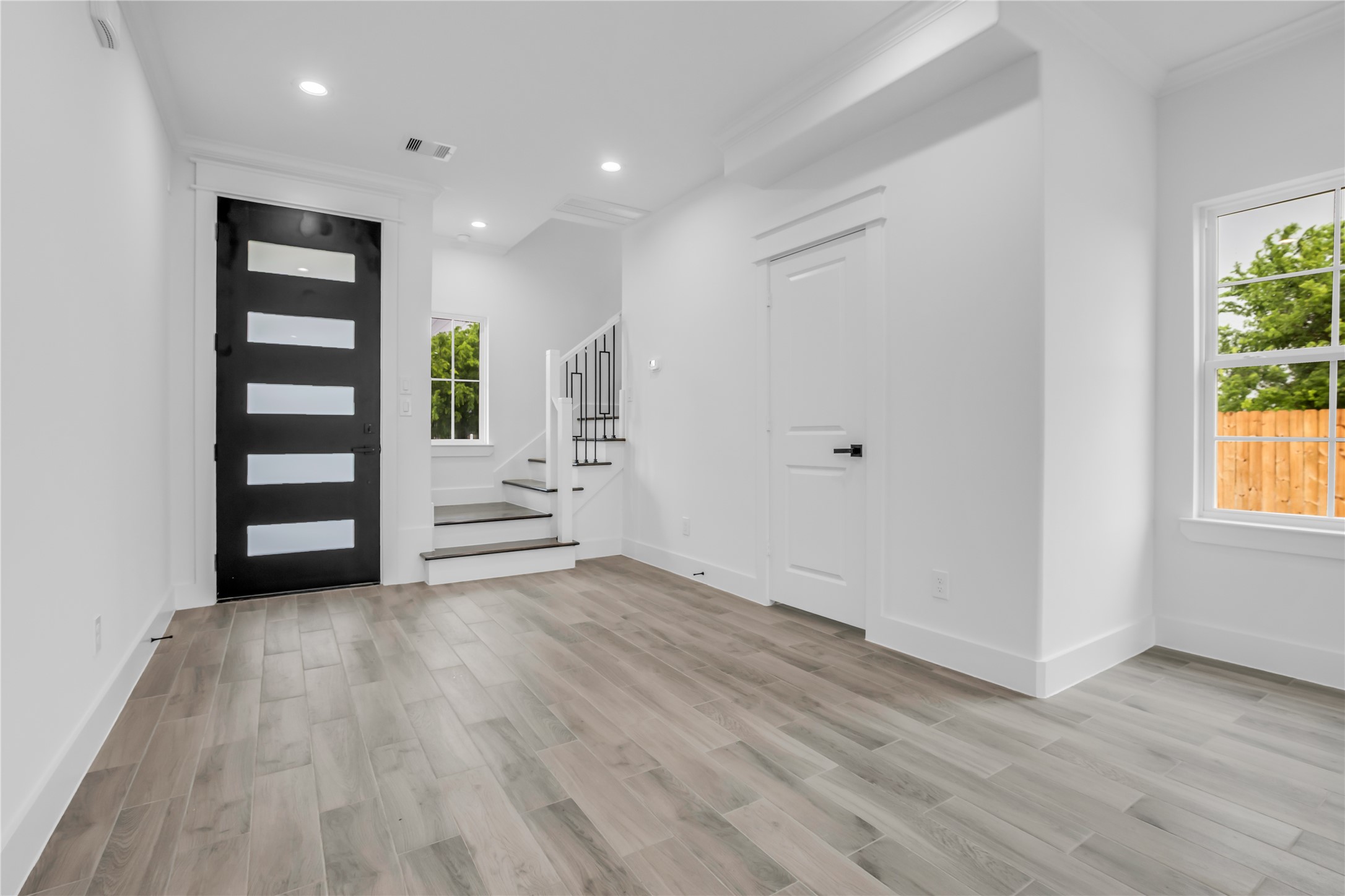 3168 Golfcrest Houston, TX 77087 - Photo 7 of 36 This modern entryway features sleek wood flooring, a stylish black door with frosted glass panels, bright white walls, and ample natural light. A staircase with white risers and dark treads adds a touch of elegance.