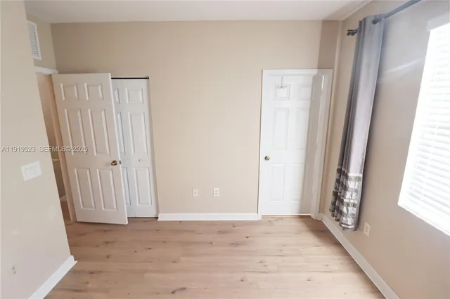 a view of an empty room with wooden floor and a window