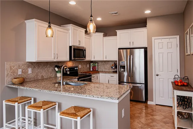 a kitchen with granite countertop a refrigerator a stove a sink dishwasher and white cabinets with wooden floor