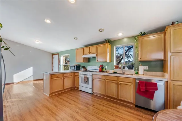 a kitchen with stainless steel appliances granite countertop a refrigerator a stove a dining table and chairs with wooden floor