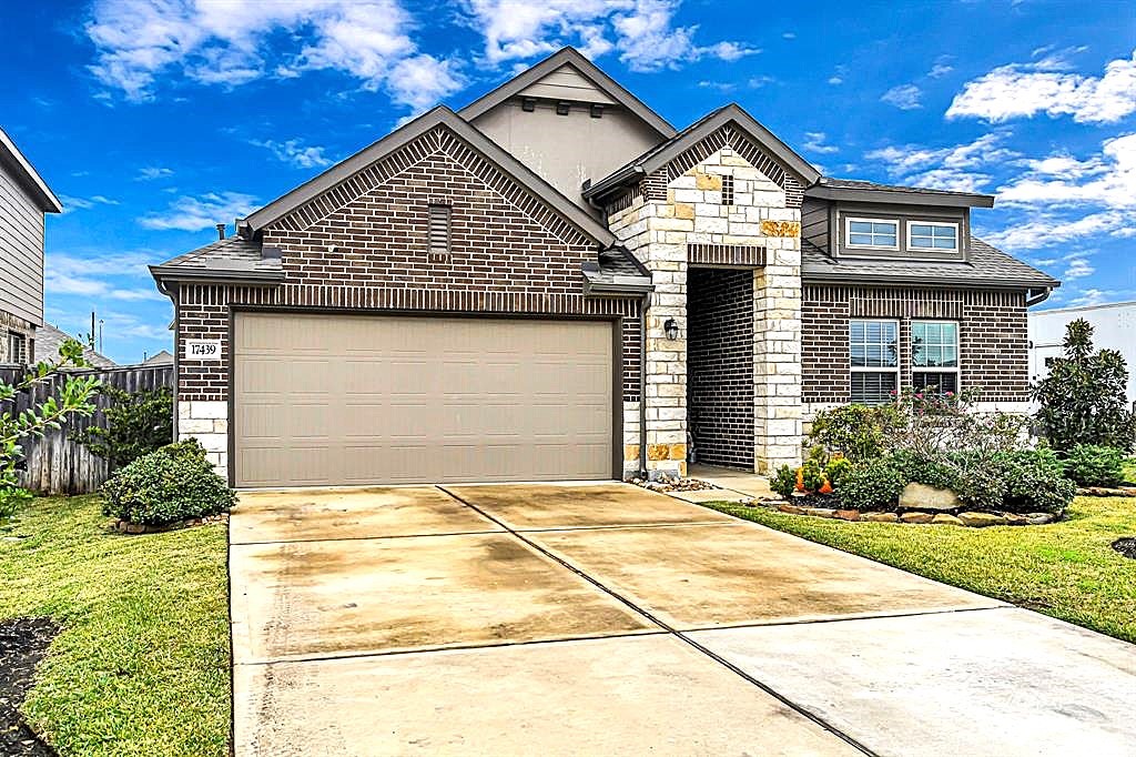 17439 Chester Valley Trail Hockley, TX 77447 - Photo 2 of 22 This home features a modern brick exterior with stone accents, a two-car garage, and a well-maintained front yard. The driveway and entryway provide a welcoming approach to the property.