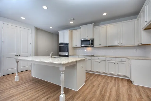 a kitchen with kitchen island white cabinets stainless steel appliances a sink and wooden floor