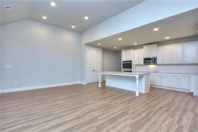a view of kitchen with kitchen island wooden floors stainless steel appliances cabinets and a center island