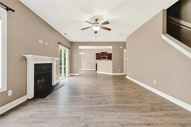 a view of a livingroom with a fireplace a ceiling fan and wooden floor