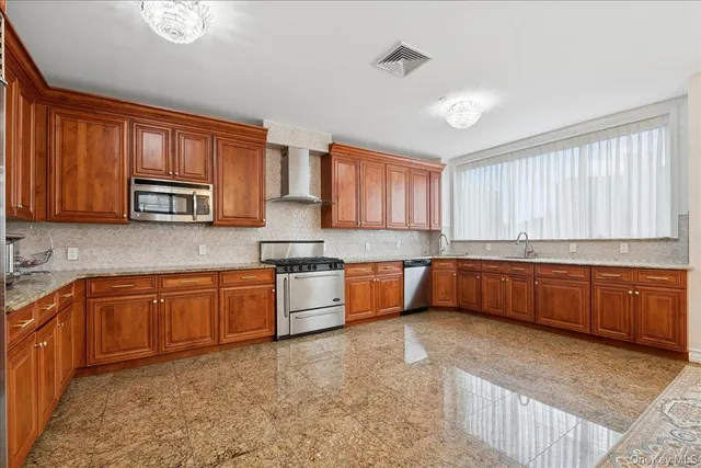 a large kitchen with stainless steel appliances granite countertop wooden cabinets a stove a sink and a window