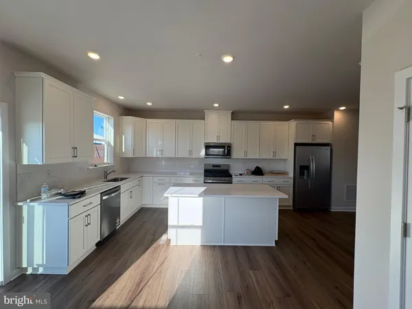 a kitchen with stainless steel appliances kitchen island granite countertop a stove top oven a sink a refrigerator and white cabinets with wooden floor