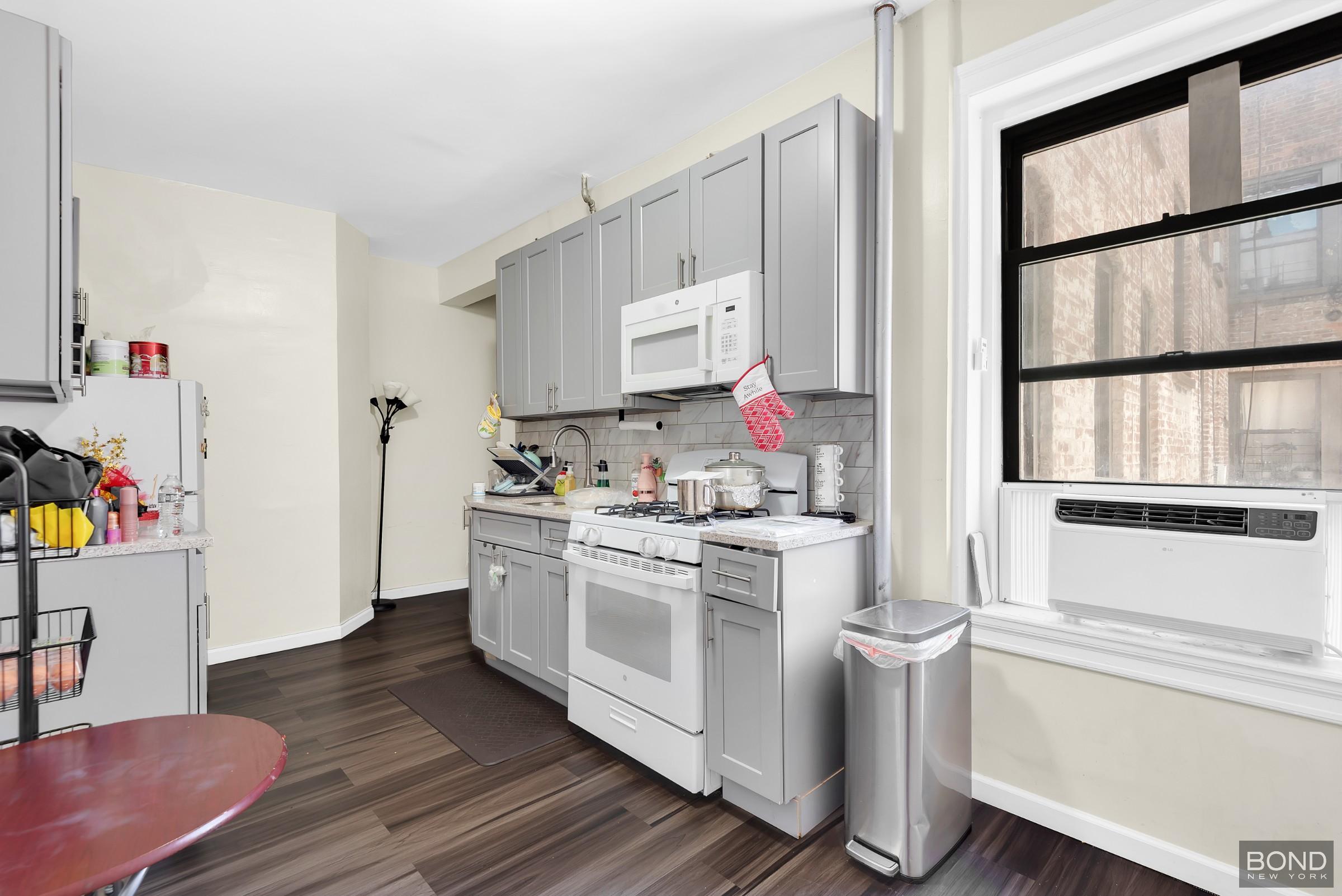 41-11 28th Avenue, Unit 1 Queens, NY 11103 - Photo 7 of 9 a kitchen with a stove and white cabinets with wooden floor