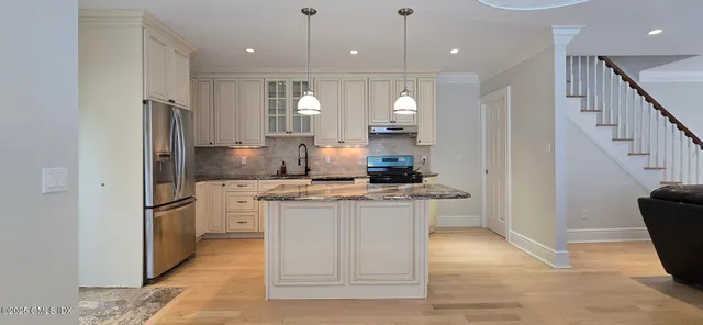 a kitchen with stainless steel appliances granite countertop a refrigerator a sink a stove and a wooden floors