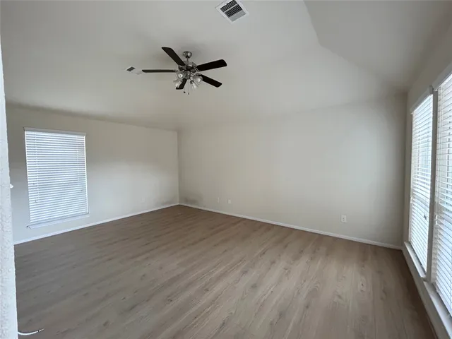 an empty room with wooden floor fan and windows