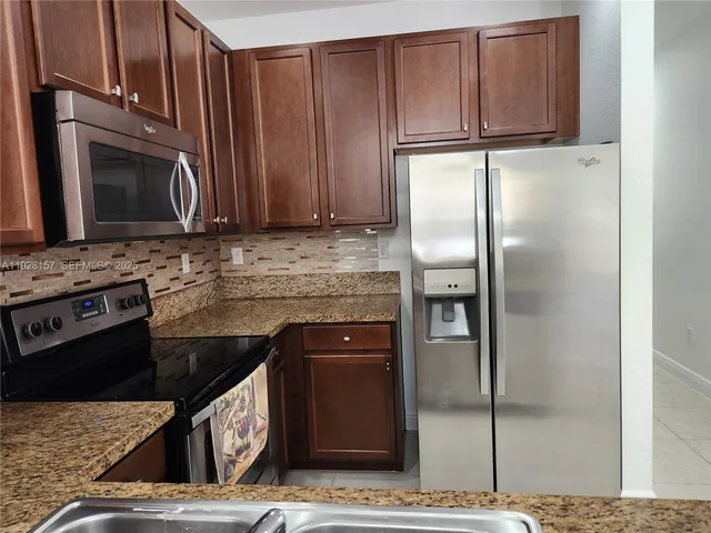 a kitchen with stainless steel appliances granite countertop a refrigerator a stove and a sink with wooden cabinets