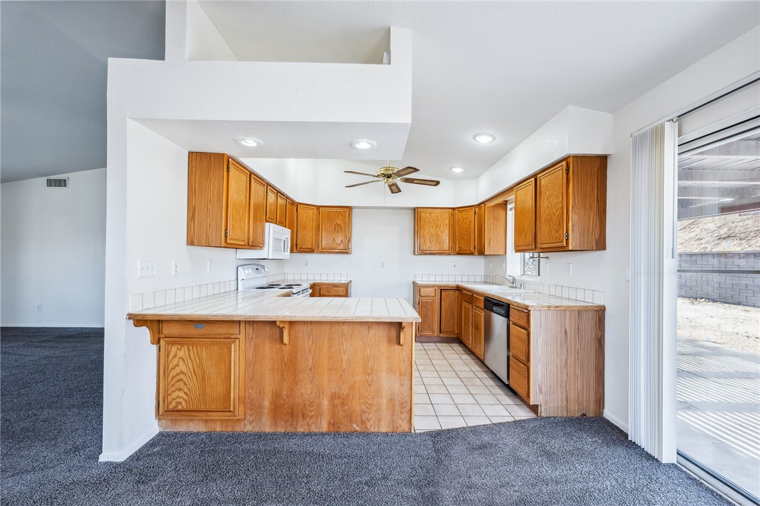 2524 South Ridge Avenue Bullhead City, AZ 86429 - Photo 19 of 64 Kitchen featuring white appliances, light carpet, a peninsula, brown cabinetry, and tile counters