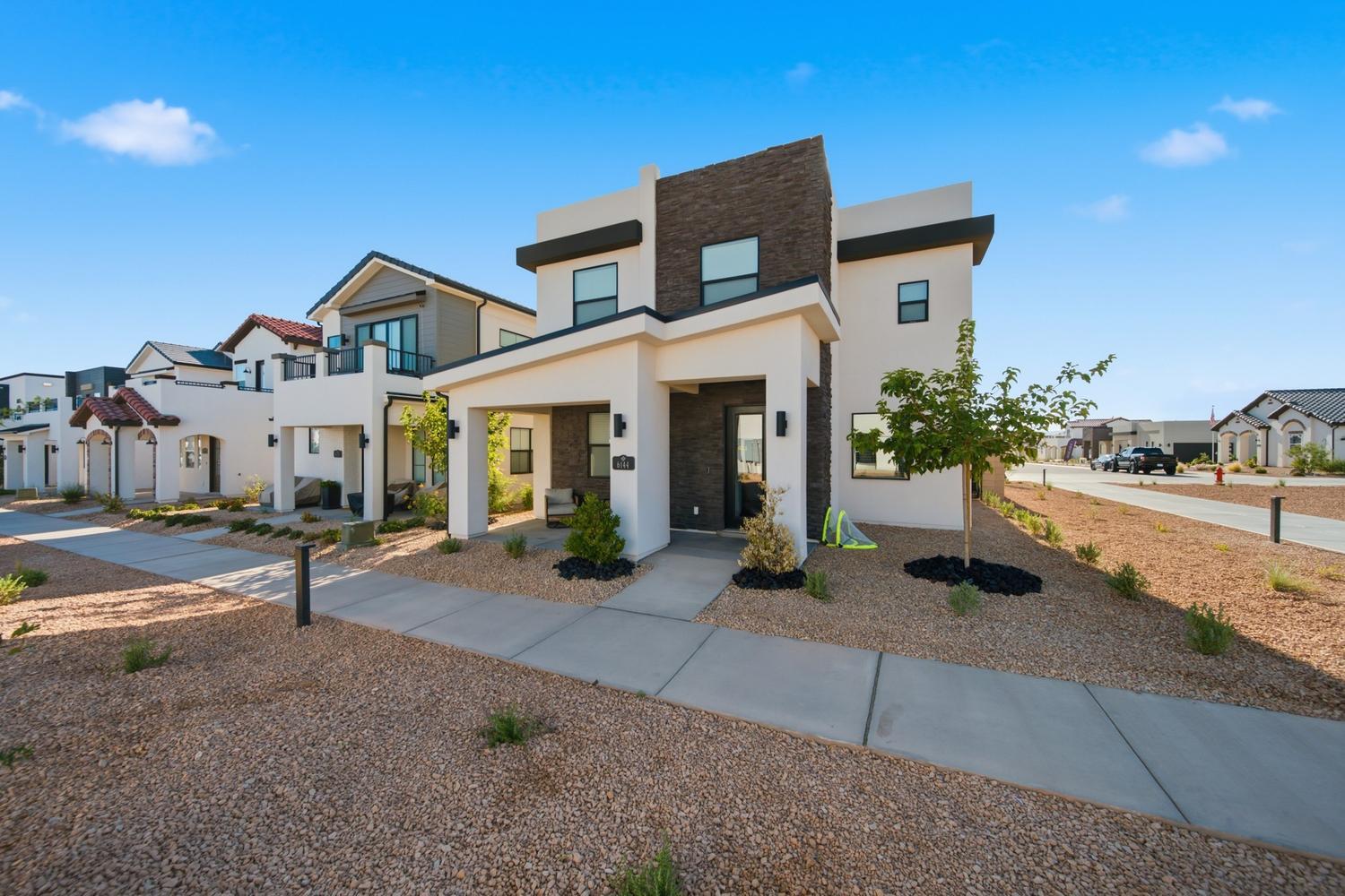 6144 Red Sand Lane St. George, UT 84790 - Photo 2 of 19 Craftsman-modern design commands attention from every angle, with a rich mix of warm stucco tones and black-framed windows. Positioned along a quiet street lined with new construction, the home offers mature desert plantings and an inviting facade that balances texture with clean geometry.
