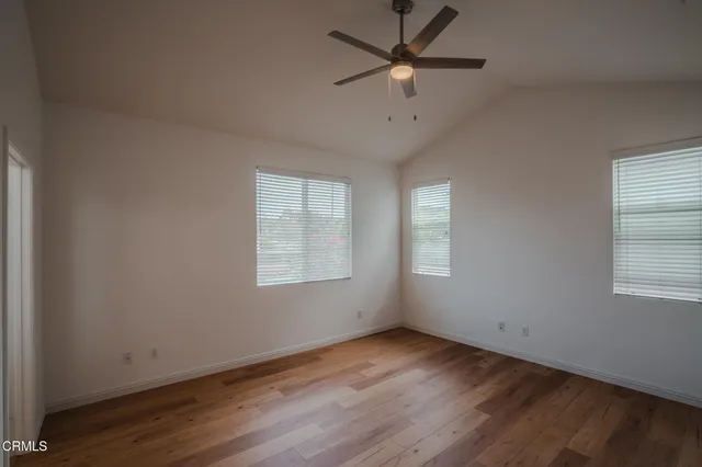 an empty room with wooden floor ceiling fan and windows