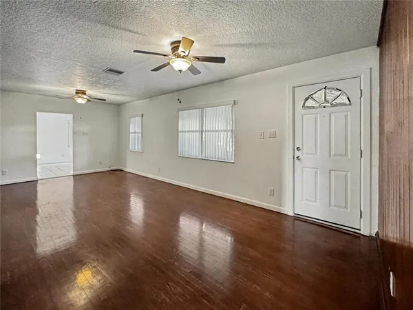 an empty room with wooden floor chandelier fan and windows