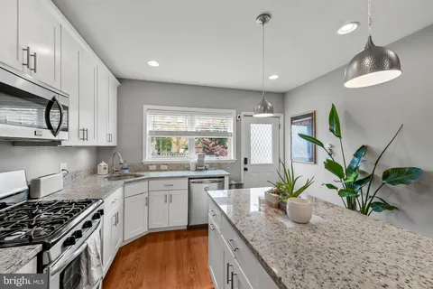 a kitchen with stainless steel appliances granite countertop a refrigerator a stove a sink a microwave a dining table and chairs with wooden floor