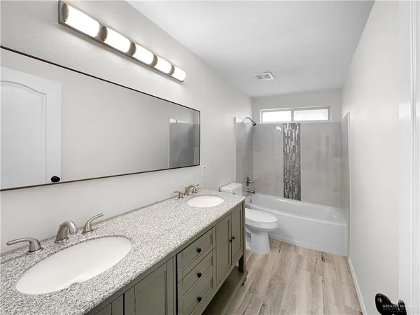 a bathroom with a granite countertop sink a toilet a mirror and shower