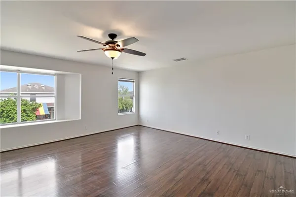 an empty room with wooden floor chandelier fan and windows