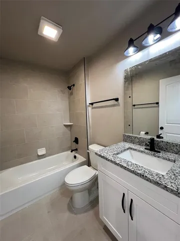 a bathroom with a granite countertop sink a toilet a mirror and bathtub
