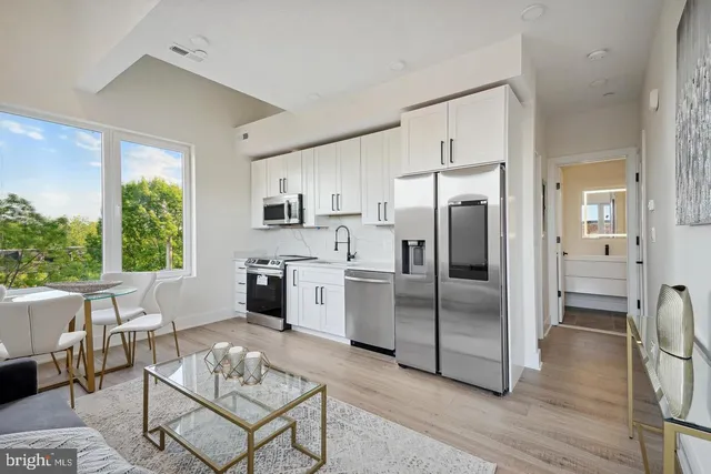 a kitchen with stainless steel appliances a refrigerator a stove a sink a dining table and chairs with wooden floor