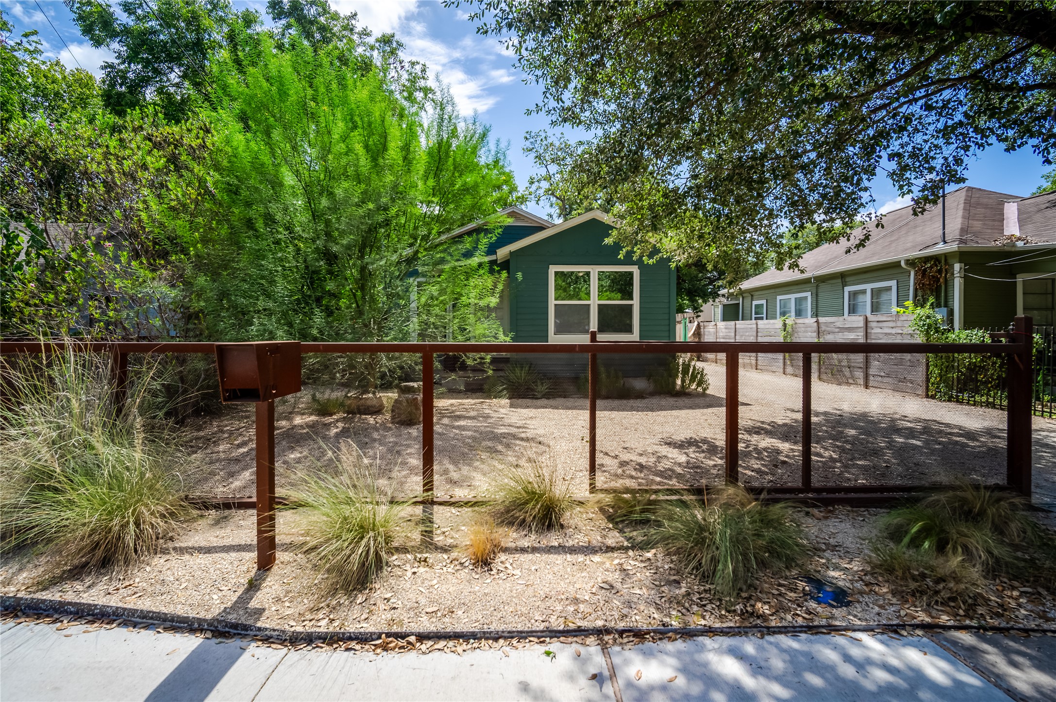 719 Springdale Road Austin, TX 78702 - Photo 4 of 17 A quaint residence sits behind a weathered steel fence, nestled amidst mature trees and a gravel yard.