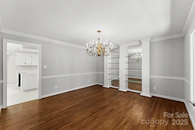 an empty room with wooden floor chandelier and windows