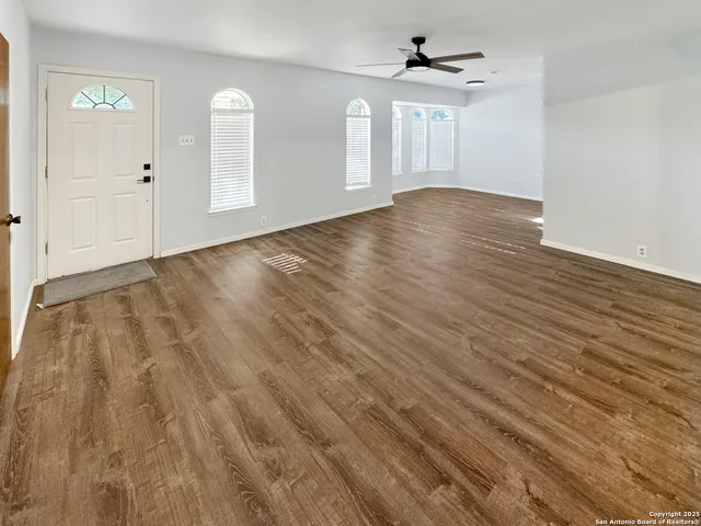 an empty room with wooden floor ceiling fan and windows