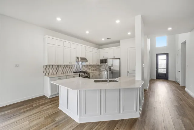 a kitchen with stainless steel appliances granite countertop a sink a stove a refrigerator and a oven with wooden floor