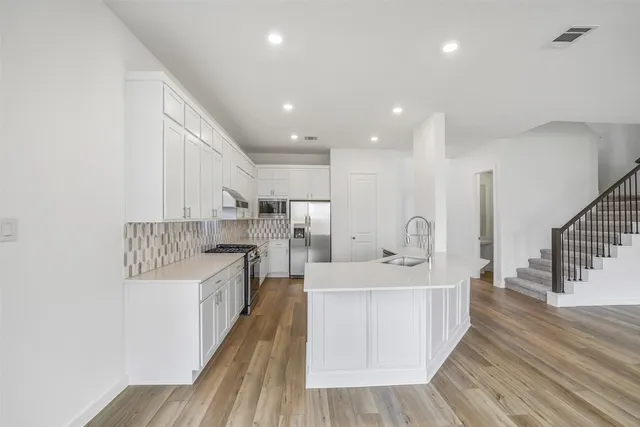 a large room with kitchen island a sink wooden floor and stainless steel appliances