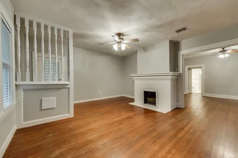 an empty room with wooden floor a fireplace a ceiling fan and windows