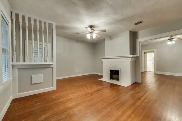 an empty room with wooden floor a fireplace a ceiling fan and windows