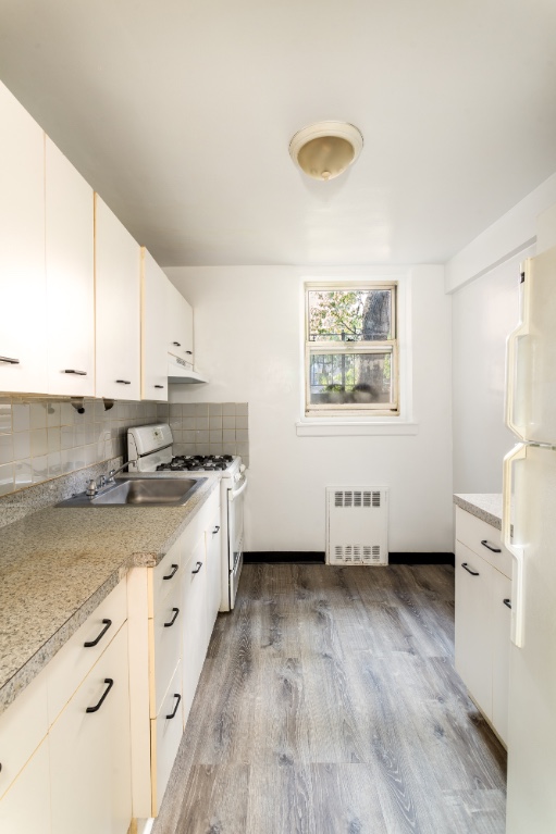 5610 Netherland Avenue, Unit 1G Bronx, NY 10471 - Photo 10 of 17 a kitchen with granite countertop a stove a sink a refrigerator and white cabinets with wooden floor