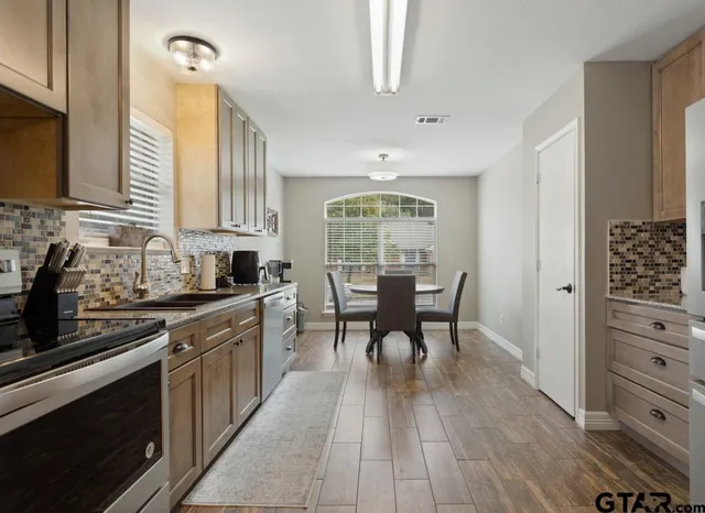 a kitchen with stainless steel appliances granite countertop a stove top oven a sink dishwasher a dining table and chairs with wooden floor