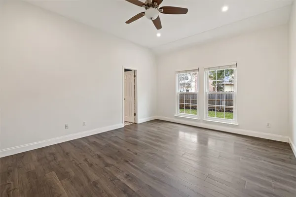 an empty room with wooden floor chandelier fan and windows