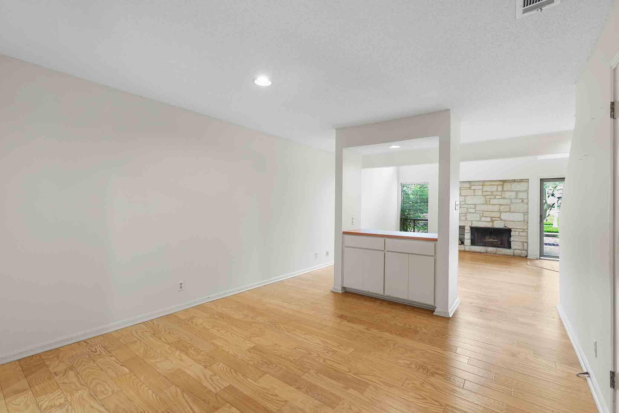 9226 Jollyville Road, Unit 132 Austin, TX 78759 - Photo 5 of 15 Blonde hardwood flooring connects an open layout with a stone fireplace and abundant natural light.